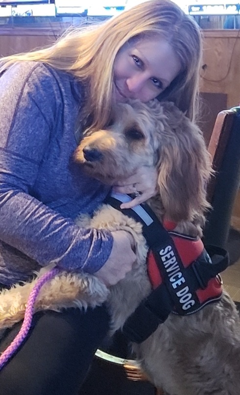 Laura holding Brandy, her personally trained diabetic alert service dog, wearing a service dog vest.
